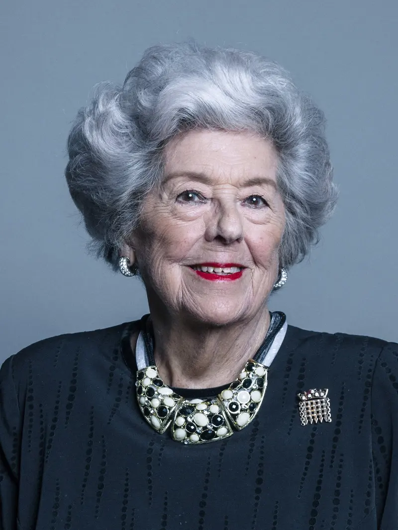 Photo of a smiling older woman with grey hair, wearing a dark jumper and a pearl necklace