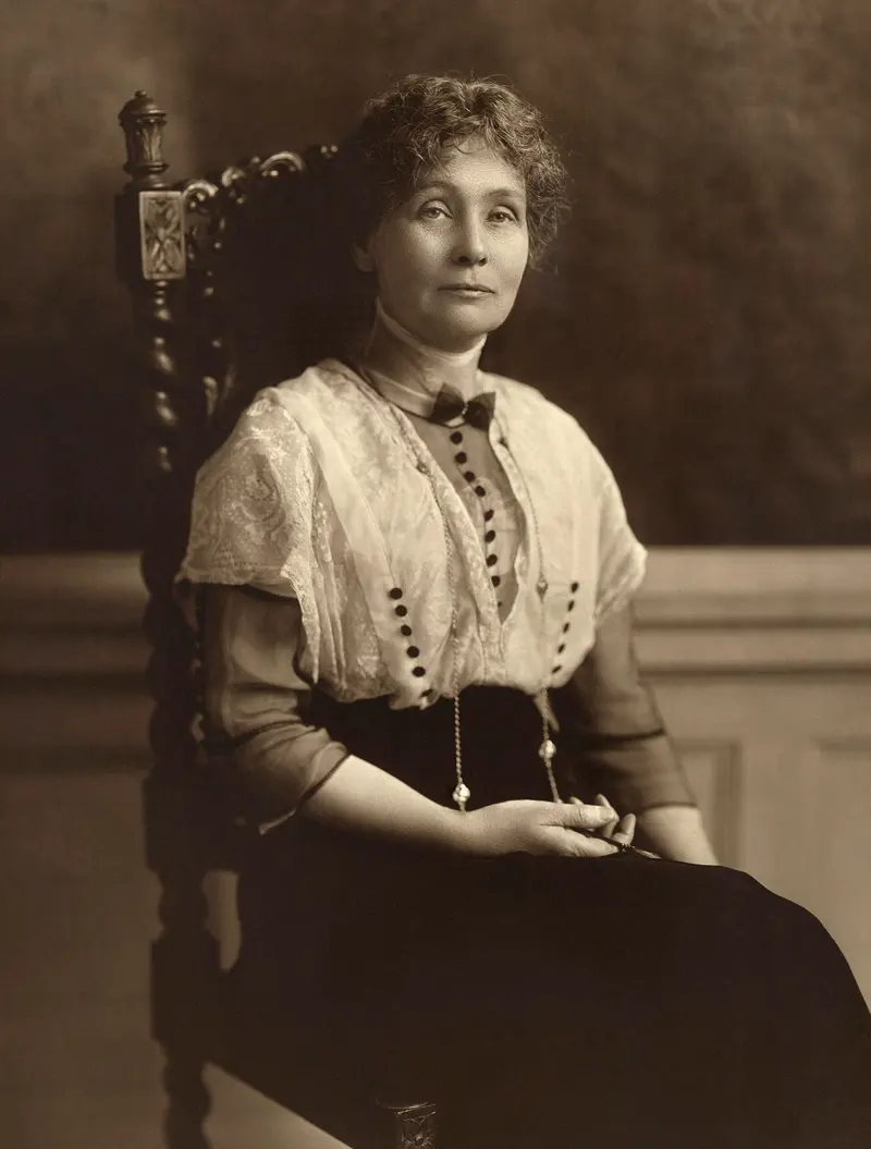 Old sepia photo of a woman with her hair pinned up, wearing a high-collared blouse and sitting in a carved chair