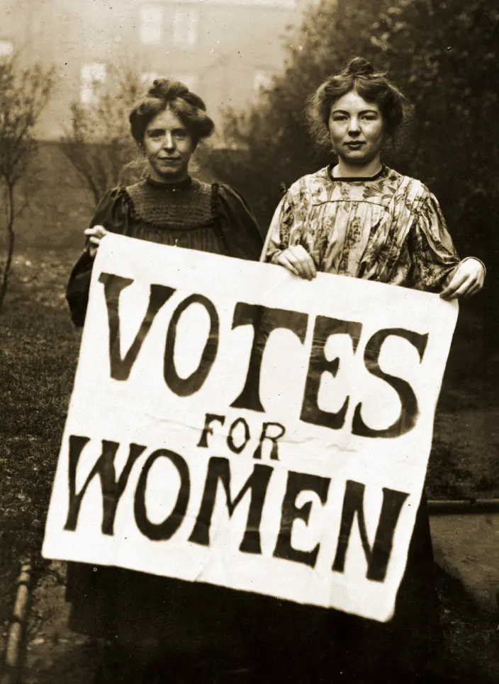 Two women holding up a large banner that says Votes for Women