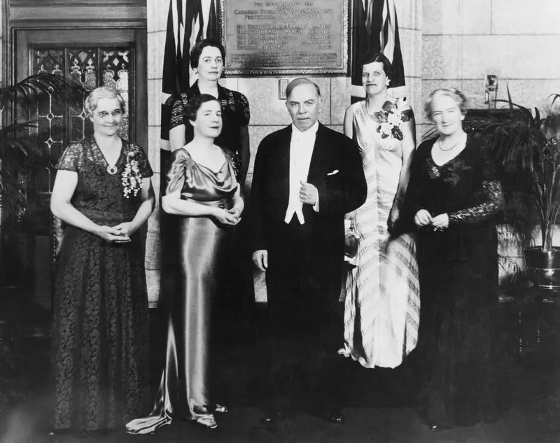 Black-and-white photo of a group of women and the Prime Minister of Canada standing beside a plaque