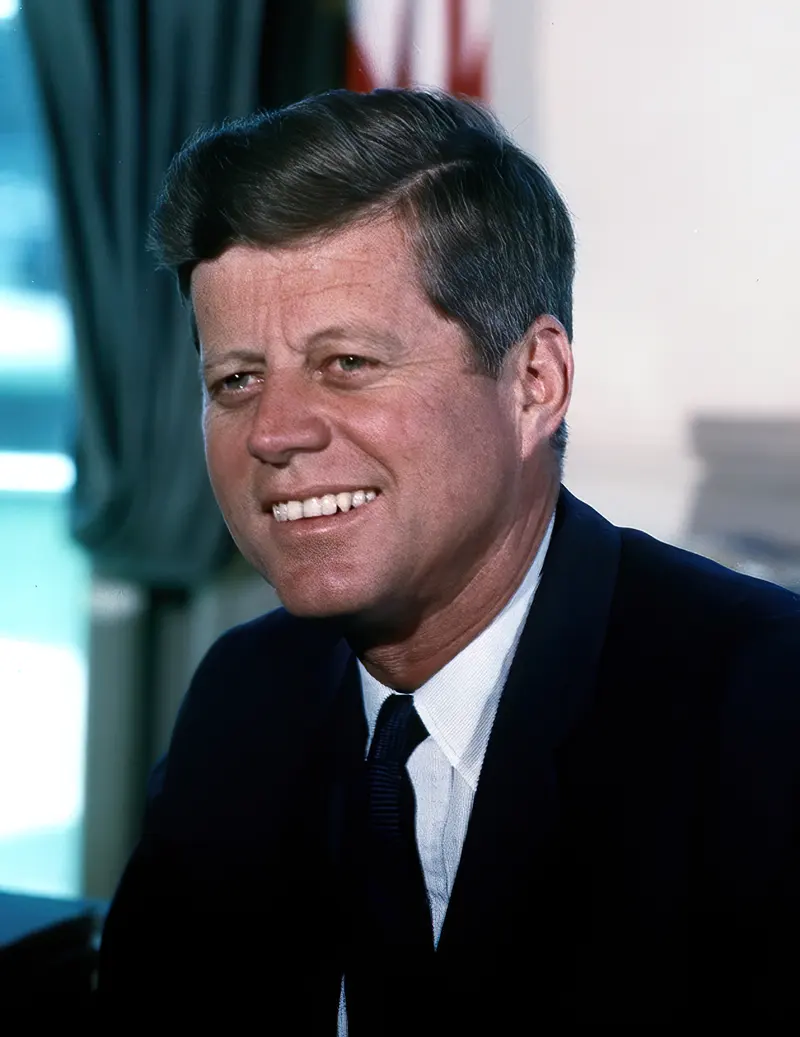 Colour photo of a smiling man with brown hair in a dark suit and tie